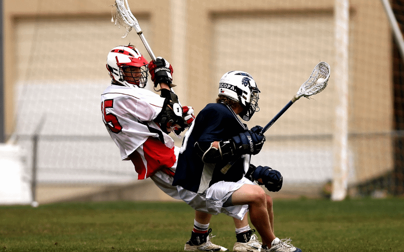 A lacrosse field with players in action, surrounded by spectators, under bright stadium lights